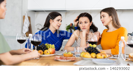 Sad Spanish woman sits silently in kitchen, female friends sympathize and comfort woman Sad Spanish woman sits silently in kitchen, female friends sympathize and comfort woman 140293002