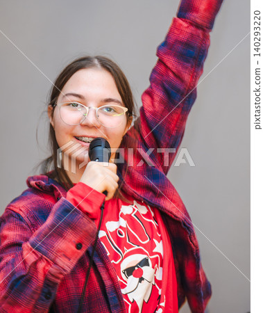 Teen Girl Singing with Raised Arm on Grey Background Teen Girl Singing with Raised Arm on Grey Background 140293220