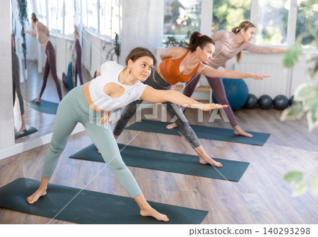 Women practicing warrior pose of yoga on mat in fitness room Women practicing warrior pose of yoga on mat in fitness room 140293298