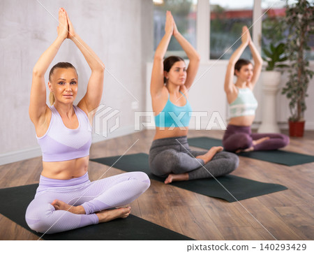 Young female yoga instructor showing others lotus pose in wellness center Young female yoga instructor showing others lotus pose in wellness center 140293429