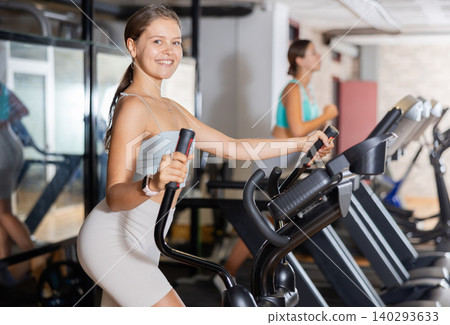 Portrait of sporty woman doing cardio workout on elliptical cross trainer at fitness center Portrait of sporty woman doing cardio workout on elliptical cross trainer at fitness center 140293633