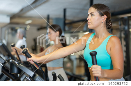 Portrait of sporty woman doing cardio workout on elliptical cross trainer at fitness center Portrait of sporty woman doing cardio workout on elliptical cross trainer at fitness center 140293732
