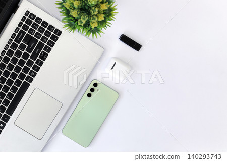 Minimalist workspace with sleek gadgets. Green phone rests beside laptop and mouse. White earbuds and pen add functional touch. Clean desk invites calm, focused productivity Minimalist workspace with sleek gadgets. Green phone rests beside laptop and mouse. White earbuds and pen add functional touch. Clean desk invites calm, focused productivity 140293743