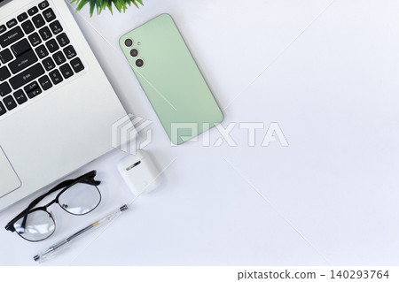 Clean desk with laptop, phone, glasses, and pen. White surface holds modern tech and accessories. Glasses sit beside keyboard, suggesting focus. Phone rests near plant, hinting at calm productivity Clean desk with laptop, phone, glasses, and pen. White surface holds modern tech and accessories. Glasses sit beside keyboard, suggesting focus. Phone rests near plant, hinting at calm productivity 140293764
