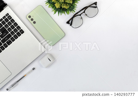 Minimalist workspace with sleek gadgets. Green phone rests beside laptop and mouse. White earbuds and pen add functional touch. Clean desk invites calm, focused productivity Minimalist workspace with sleek gadgets. Green phone rests beside laptop and mouse. White earbuds and pen add functional touch. Clean desk invites calm, focused productivity 140293777