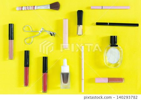 Bright yellow background with assorted makeup tools. Brushes, eyeliner, lipstick, and a small bottle are scattered. Each item is neatly placed for easy viewing Bright yellow background with assorted makeup tools. Brushes, eyeliner, lipstick, and a small bottle are scattered. Each item is neatly placed for easy viewing 140293782