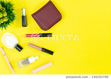 Bright yellow background with beauty items arranged neatly. Small green plant adds fresh, natural contrast. Compact wallet and makeup tools sit beside lip glosses Bright yellow background with beauty items arranged neatly. Small green plant adds fresh, natural contrast. Compact wallet and makeup tools sit beside lip glosses 140293790