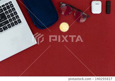 Red surface holds tech and accessories. Laptop, phone, earbuds, and sunglasses rest nearby. Small plant adds green contrast to bold red. Cozy, stylish, modern scene for digital lifestyles Red surface holds tech and accessories. Laptop, phone, earbuds, and sunglasses rest nearby. Small plant adds green contrast to bold red. Cozy, stylish, modern scene for digital lifestyles 140293817