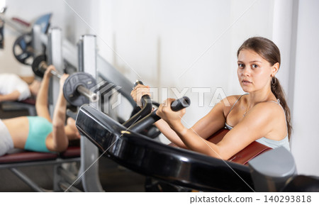 Slender athletic girl work out muscles of arms and shoulders on simulator in gym of fitness club Slender athletic girl work out muscles of arms and shoulders on simulator in gym of fitness club 140293818