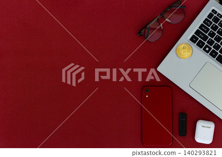 Red surface holds tech and accessories. Laptop, phone, earbuds, and sunglasses rest nearby. Small plant adds green contrast to bold red. Cozy, stylish, modern scene for digital lifestyles 140293821