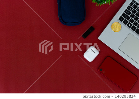Red surface holds tech and accessories. Laptop, phone, earbuds, and sunglasses rest nearby. Small plant adds green contrast to bold red. Cozy, stylish, modern scene for digital lifestyles 140293824