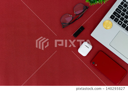Red surface holds tech and style items. Laptop, phone, earbuds, and glasses create modern vibe. Golden coin adds digital finance touch. Minimalist layout invites creative use Red surface holds tech and style items. Laptop, phone, earbuds, and glasses create modern vibe. Golden coin adds digital finance touch. Minimalist layout invites creative use 140293827