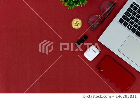 Red surface holds tech and style items. Laptop, phone, earbuds, and glasses create modern vibe. Golden coin adds digital finance touch. Minimalist layout invites creative use Red surface holds tech and style items. Laptop, phone, earbuds, and glasses create modern vibe. Golden coin adds digital finance touch. Minimalist layout invites creative use 140293831