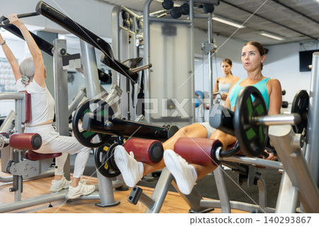Slender athletic girl work out muscles of legs and thighs on simulator in fitness club Slender athletic girl work out muscles of legs and thighs on simulator in fitness club 140293867