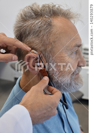 Hearing solutions. Audioprosthetist adjusts senior patient's hearing aids using special equipment, and takes real ear measurements 140293879