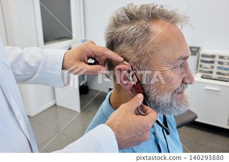 Audiologist carefully adjusts a hearing aid on elderly man using advanced audiological equipment for personalized fitting, side view 140293880