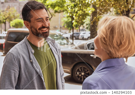 Handsome man with hearing impairment uses hearing aid to communicate with his female colleague outdoor in noise city. Hearing solutions 140294103