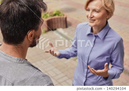 Lively discussion occurs outside as adult male with a hearing aid joyfully connects with woman friend amidst urban sounds Lively discussion occurs outside as adult male with a hearing aid joyfully connects with woman friend amidst urban sounds 140294104
