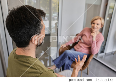 Handsome man with hearing aid enjoys conversation with woman, showcasing effective communication. Living a full life with modern hearing technology Handsome man with hearing aid enjoys conversation with woman, showcasing effective communication. Living a full life with modern hearing technology 140294138