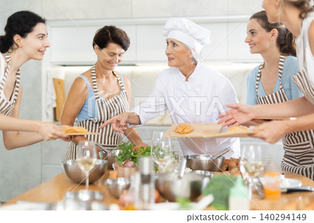 Elderly female chef holds and tells students of culinary courses about unusual marinade for poultry Elderly female chef holds and tells students of culinary courses about unusual marinade for poultry 140294149