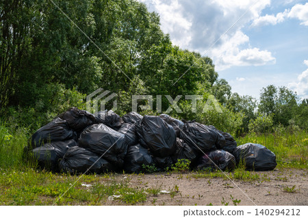 Large pile of black trash bags sits on a grassy dirt area.\nLitter Large pile of black trash bags sits on a grassy dirt area.\nLitter 140294212