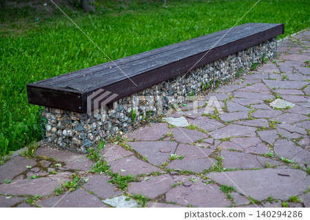 Dark wooden bench rests on a stone base Dark wooden bench rests on a stone base 140294286