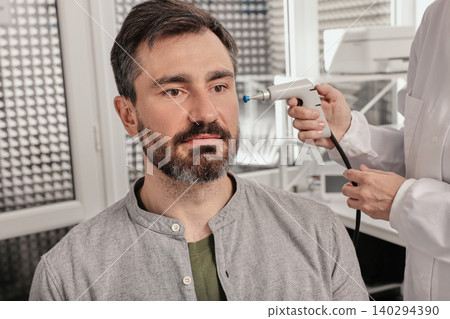 Portrait of handsome man while tympanometry and test of middle-ear function with ENT-doctor using tympanometer probe at hearing center, close-up Portrait of handsome man while tympanometry and test of middle-ear function with ENT-doctor using tympanometer probe at hearing center, close-up 140294390
