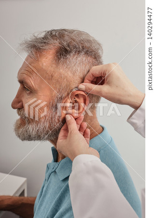Audiologist installing hearing aid on ear of elderly man in hearing clinic. Deafness Treatment, hearing solutions 140294477