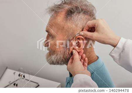 Installation hearing aid on senior man's ear at hearing clinic, close-up, side view. Deafness treatment, hearing solutions 140294478