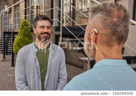 Two friends chat in a busy city, using a hearing aid for clear communication amid the noise Two friends chat in a busy city, using a hearing aid for clear communication amid the noise 140294509