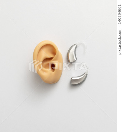 Detailed top view showcases a hearing aid set beside model of silicone ear, lying on doctor table in audiology. Hearing loss concept Detailed top view showcases a hearing aid set beside model of silicone ear, lying on doctor table in audiology. Hearing loss concept 140294661