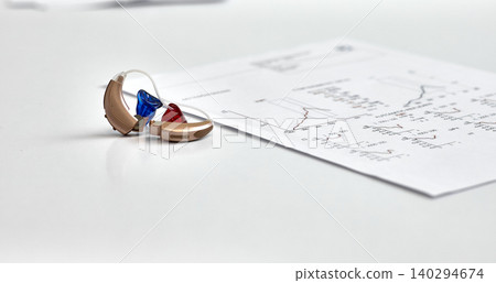 Left and right hearing aids lying on audiologist table near hearing test documents. Hearing check-up concept Left and right hearing aids lying on audiologist table near hearing test documents. Hearing check-up concept 140294674