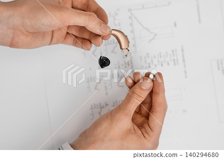 Hands showcase a small hearing aid and battery to it, emphasizing its importance in enhancing communication and daily life experience Hands showcase a small hearing aid and battery to it, emphasizing its importance in enhancing communication and daily life experience 140294680