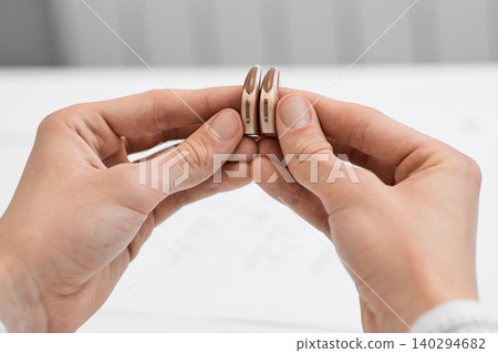 Audiologist carefully examine a pair of sleek hearing aids designed for improved auditory clarity and comfort Audiologist carefully examine a pair of sleek hearing aids designed for improved auditory clarity and comfort 140294682