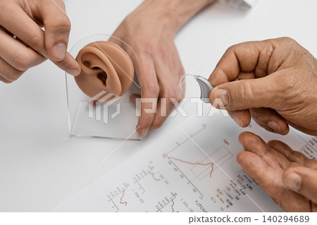 Client learns about hearing aids while examining ear anatomy with a professional at an audiologist office. Hearing solutions Client learns about hearing aids while examining ear anatomy with a professional at an audiologist office. Hearing solutions 140294689