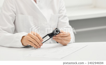 Expert audiologist prepares for a consultation in medical office, focusing on patient care with otoscope in hand. Hearing clinic Expert audiologist prepares for a consultation in medical office, focusing on patient care with otoscope in hand. Hearing clinic 140294694