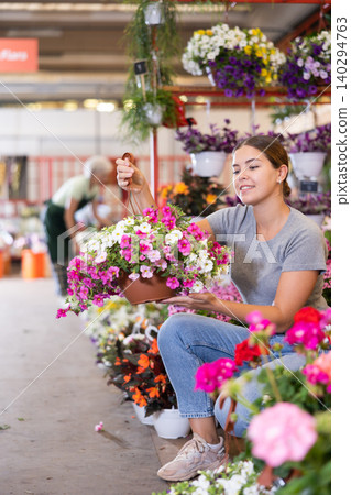 Focused young female consumer in casual wear choosing petunia flower in pot while buying plants in market Focused young female consumer in casual wear choosing petunia flower in pot while buying plants in market 140294763