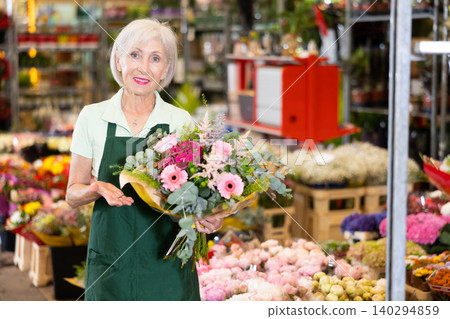 Old saleswoman holding bouquet of flowers in open-air plants market 140294859