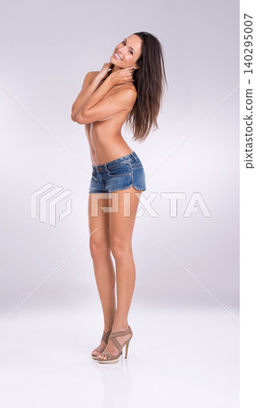 Portrait, smile and denim shorts with woman in studio on gray background for feminine confidence. Fashion, sexy and shirtless with body of happy young model in jeans for style or natural sensuality 140295007