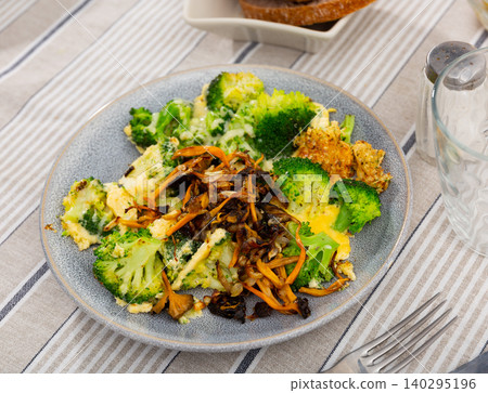 There is stewed broccoli and pickled wild mushrooms chanterelle on plate. There is stewed broccoli and pickled wild mushrooms chanterelle on plate. 140295196