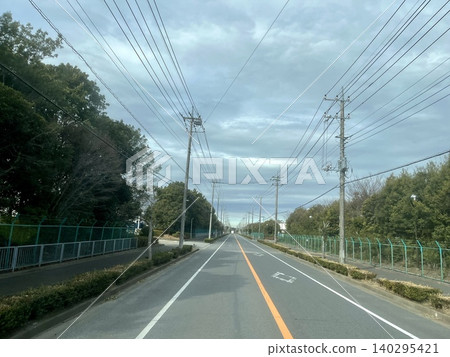 一條筆直的郊區道路,兩旁林立著電線桿和輸電線路,天空陰雲密布。 一條筆直的郊區道路,兩旁林立著電線桿和輸電線路,天空陰雲密布。 140295421