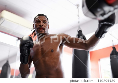 Man, boxing and bag with gloves for fitness or strong practice or fight competition, training or challenge. Black person, sweat and gym workout or exercise in Nigeria or confident, muscle or combat Man, boxing and bag with gloves for fitness or strong practice or fight competition, training or challenge. Black person, sweat and gym workout or exercise in Nigeria or confident, muscle or combat 140295589