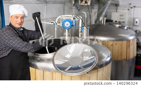 Brewery worker stirring raw materials in fermenter for beer production Brewery worker stirring raw materials in fermenter for beer production 140296324
