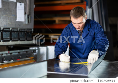 Portrait of worker with tape measure who measures sheet of iron using tape measure and marks cutting line Portrait of worker with tape measure who measures sheet of iron using tape measure and marks cutting line 140296654
