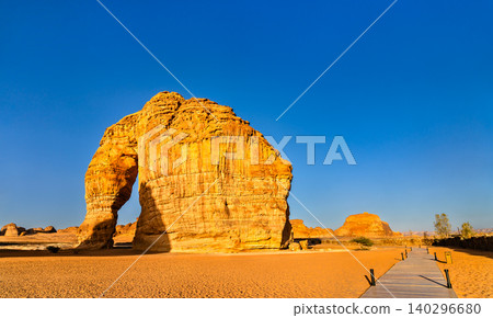 The massive Elephant Rock, also known as Jabal AlFil, standing in the desert of Al Ula, Saudi Arabia, featuring a wooden walkway in the foreground under a clear blue sky. 140296680