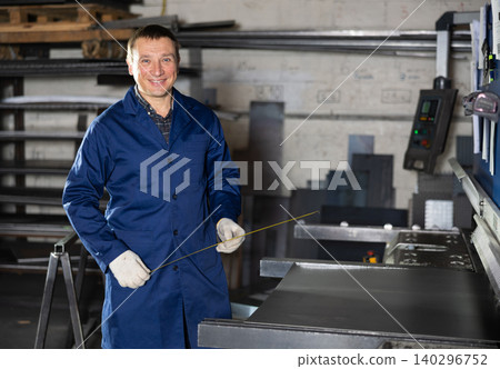 Portrait of worker with tape measure who measures sheet of iron using tape measure and marks cutting line 140296752