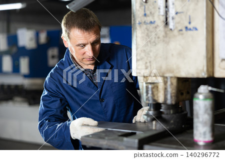 Adult man cuts holes in metal on machine Adult man cuts holes in metal on machine 140296772
