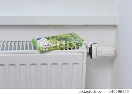 Stack of 100 euro banknotes on a home radiator symbolizing rising heating expenses, energy crisis, gas price increases, inflation and household utility costs in Europe Stack of 100 euro banknotes on a home radiator symbolizing rising heating expenses, energy crisis, gas price increases, inflation and household utility costs in Europe 140296863