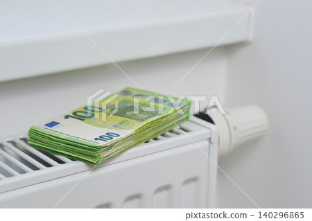 Stack of 100 euro banknotes on a home radiator symbolizing rising heating expenses, energy crisis, gas price increases, inflation and household utility costs in Europe Stack of 100 euro banknotes on a home radiator symbolizing rising heating expenses, energy crisis, gas price increases, inflation and household utility costs in Europe 140296865