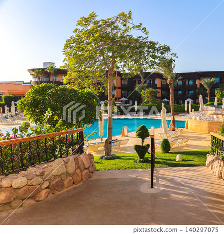 Luxurious Hotel Courtyard with Lush Greenery and Sunlit Swimming Pool Under Bright Summer Sky Luxurious Hotel Courtyard with Lush Greenery and Sunlit Swimming Pool Under Bright Summer Sky 140297075